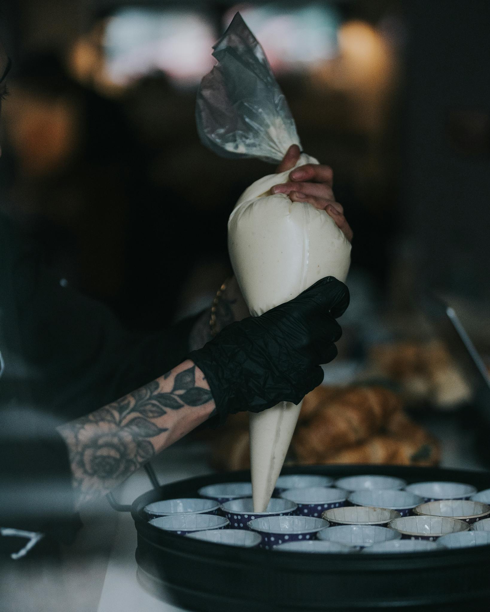 A baker expertly uses a pastry bag to prepare cupcakes in a kitchen.